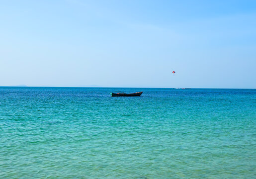 Small wooden boat floating on turquoise sea under clear blue sky with distant parasail and faint coastline