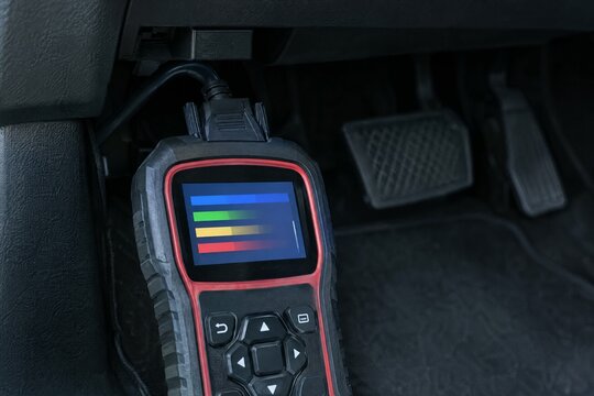 Handheld car diagnostic scan tool plugged into OBD port under dashboard