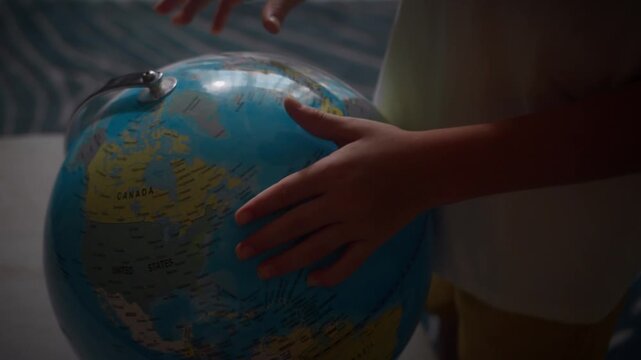 Child studying world map on globe pointing finger at Canada country