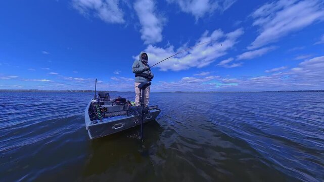 Unrecognizable man casting rod and spinning fishing reel on small fishing boat. Sport fishing leisure. Man is fishing in a boat on the lake. Angler is catching fish from powerboat in the open water.