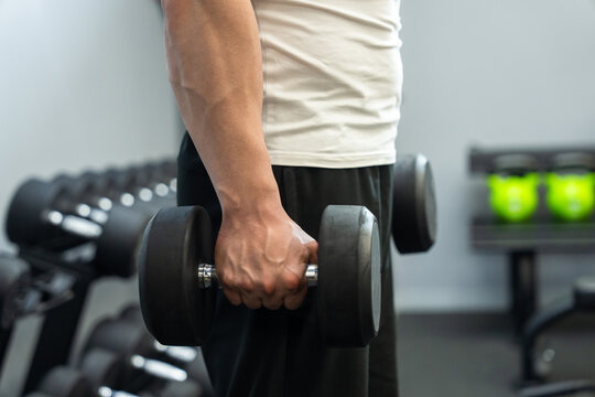 Muscular male trainer lifts dumbbells and performs biceps exercise in the gym.