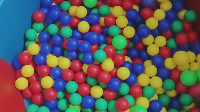 Vibrant ball pit filled with red, blue, green, and yellow plastic balls moving around. Fun concept for a children's playground or party