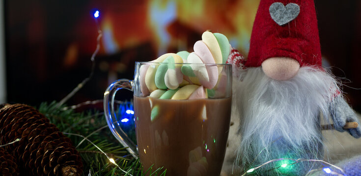 Christmas Banner for Website Header with Cute Nordic Gnome, Glass Mug of Cocoa with Marshmallows, Pine Cone and Garland Lights near Glowing Fireplace, Free Space for Text