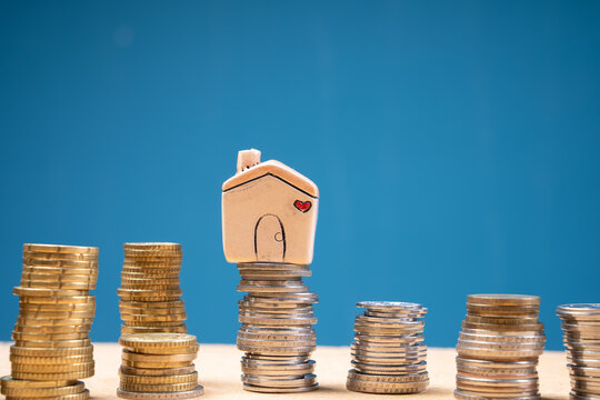 Coins stacked in piles with a miniature house on top