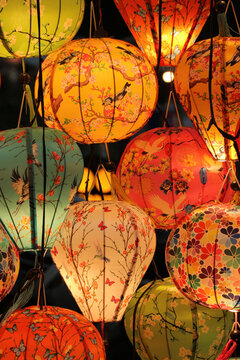 Close up of illuminated traditional Vietnamese silk lanterns with hand-painted floral and bird patterns hanging at night in Hoi An, Vietnam.