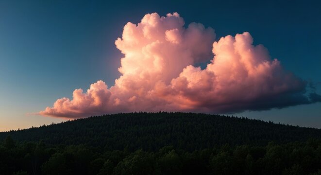 Pink-hued cumulus cloud dominates sunset sky over dark, silhouetted hilltop forest