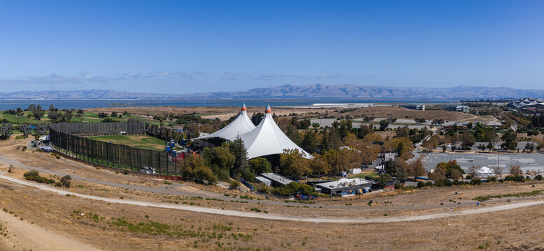 Aerial view of Googleplex Shoreline Amphitheatre and the surrounding regional park lands in Mountain View, California, showing tent structures, hills, golf course, and the bay.