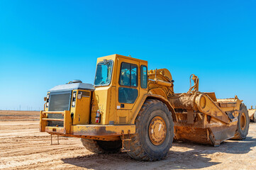 Fototapeta premium Yellow scraper stands on construction site under blue sky. Heavy construction machinery.