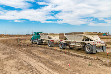 Dump truck with double trailer parked at construction site under blue sky with white clouds. © Todayphoto