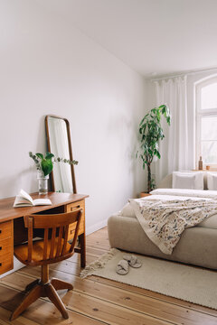 Bedroom with vintage wooden desk, chair, and large houseplant