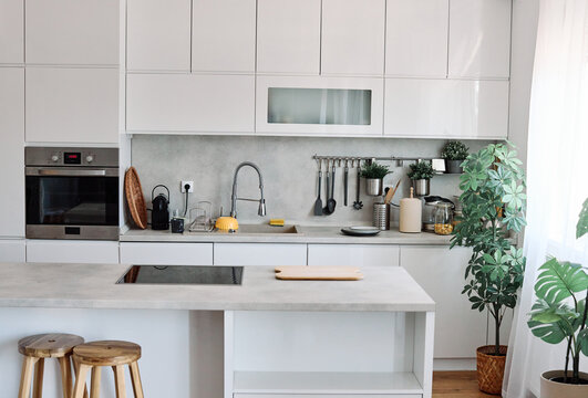 A bright modern kitchen with a central island, stainless appliances and indoor plants creating a fresh, minimal space for teen cooking, casual meals and socializing. White cabinetry, concrete countert