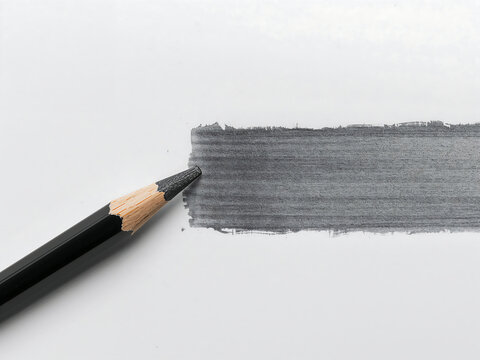 A black wooden pencil a thick horizontal line of grey graphite on a plain white paper surface, close up view of artistic tool