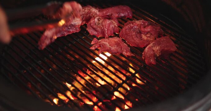 A man puts pieces of raw meat on the grill of a round grill, hot coals under the grill, and an egg-shaped grill.