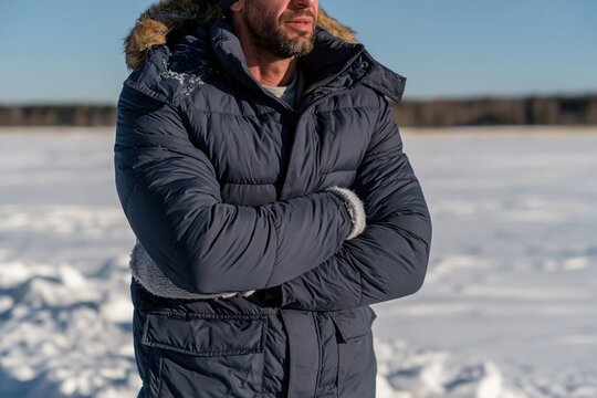 Man in a padded jacket shivering and hugging his arms in a snowy field, unposed and freezing for winter clothing and health features