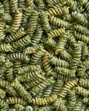 Fusilli pasta coated in pesto with an oily texture and herb flecks, creating a dense spiral pattern for pasta packaging and recipe backgrounds