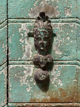 Weathered metal face-shaped door knocker on green door panel