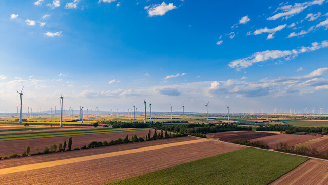 Wind turbines scattered across agricultural fields at sunset. High angle shot of multiple wind turbines placed across agricultural farmland during late afternoon light.