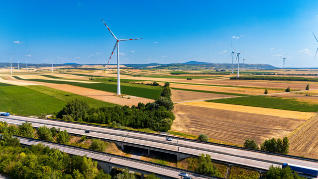 Wind turbine and highway bridge over farmland fields. High angle view of a wind turbine standing next to a highway bridge crossing agricultural fields.