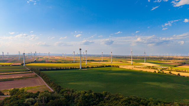 Large wind farm in rural farmland under blue sky. Panoramic aerial view of a large wind farm spread over green and yellow agricultural fields.