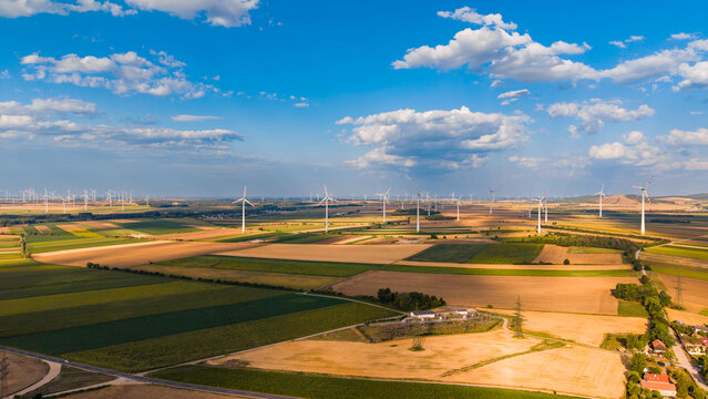 Aerial view of wind farm in green fields under cloudy sky. Aerial view of wind turbines spread across green farmland with scattered shadows from clouds.
