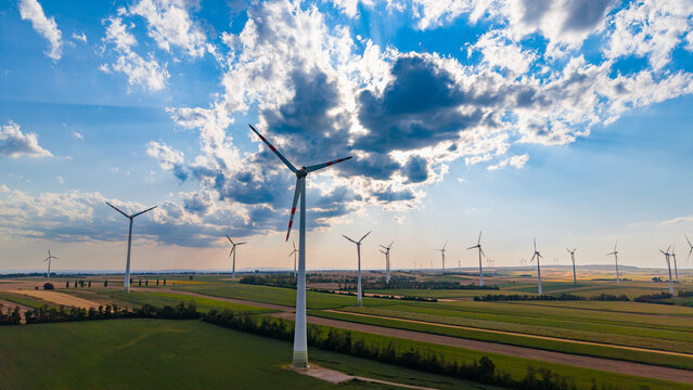 Wind turbine close up view over farmland landscape. Low altitude perspective highlights central tall industrial structure surrounded by distant identical towers.