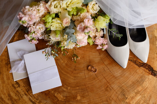 Elegant bride accessories flat lay on wooden slab background, white shoes, wedding rings, invitations, bouquet showcasing romance, quiet luxury, minimalist trends. Bride's morning concept, wedding day