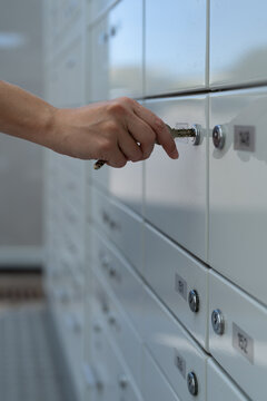 A close-up photo of a female hand inserting a key into the lock of her post office box.