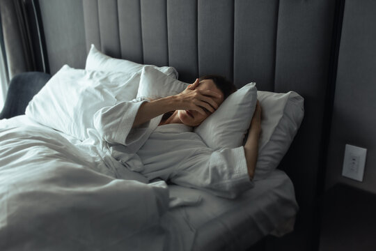 Exhausted woman waking up in bed covering her face with hand after a sleepless night
