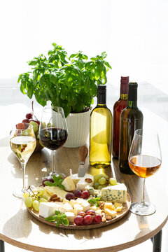 Wine and cheese platter with grapes, basil plant, and assorted bottles served on a wooden table setting
