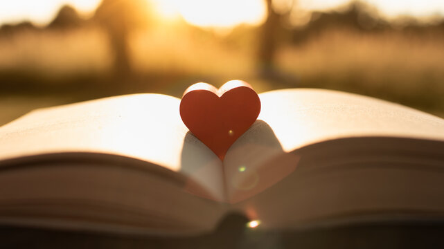 Red heart resting on open Bible book in warm sunset light symbolizing love, faith, hope and devotion
