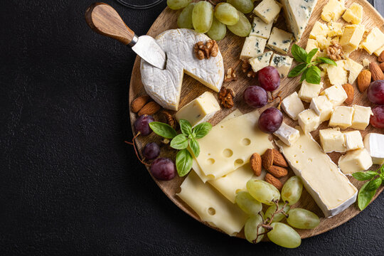 Delicious assortment of cheese grapes nuts and basil on a wooden board served on dark textured background