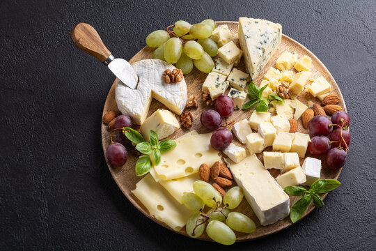 Abundant gourmet cheese board presentation with grapes almonds and fresh basil leaves