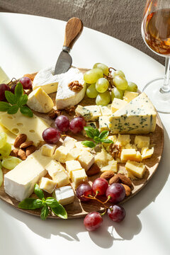 Assortment of gourmet cheeses with grapes nuts and a glass of rose wine