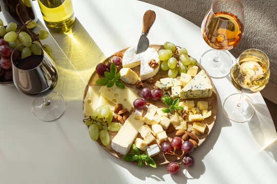 Assortment of delicious cheeses with grapes and wine presented on wooden board with glasses