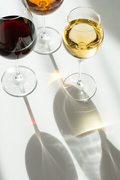 Three wine glasses with red white and amber liquids casting shadows on white background studio shot