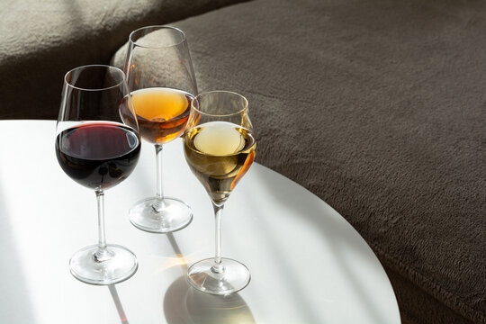 Three wine glasses filled with red white and amber beverages sit on white surface with shadow play