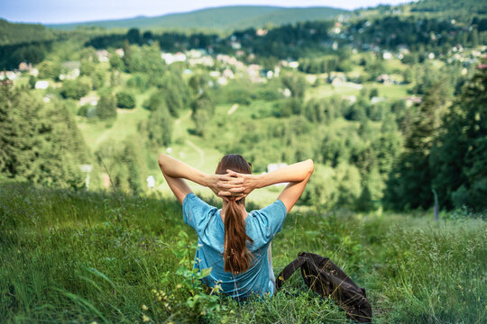 Woman relaxing on mountain hillside overlooking green valley, mindfulness, freedom, wellness, peaceful nature and outdoor adventure concept
