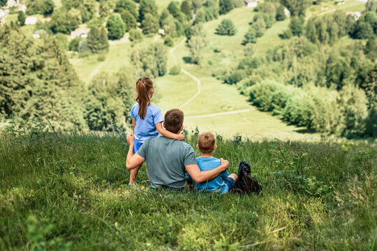 Father and two children relaxing together on mountain hillside, family bonding, fatherhood, parenting, childhood and outdoor adventure concept
