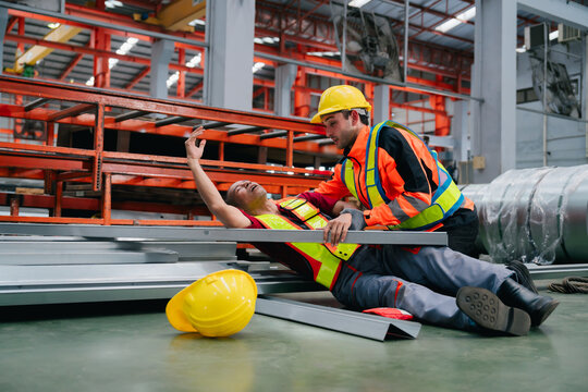 Stressed industry engineer helping worker falling on metal sheet in factory floor with panicked expression and urgent emergency situation