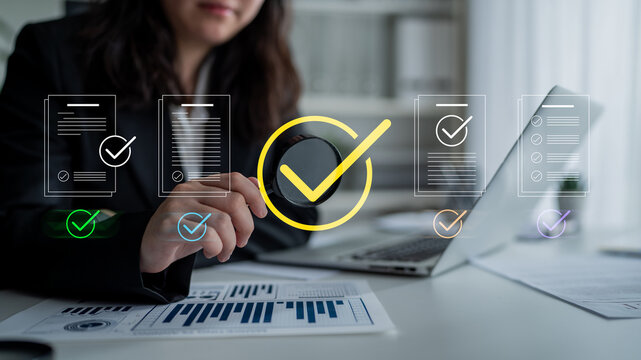 A focused business professional examines documents with digital checkmarks on a laptop. This image represents productivity, organization, and efficient workflow in a modern office environment. Cyphers
