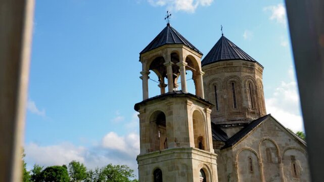 Beautiful nikortsminda cathedral, a medieval georgian orthodox church, reveals its stunning ancient architecture through a wooden fence on a sunny day with blue skies and white clouds
