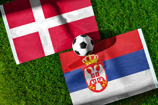 Denmark vs. Serbia football match. National flags on green grass with soccer ball in the middle. Football background for international match.