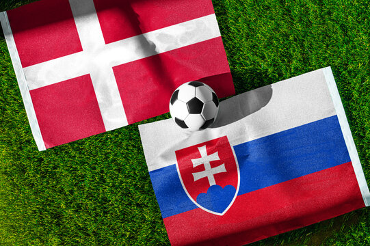 Denmark vs. Slovakia football match. National flags on green grass with soccer ball in the middle. Football background for international match.
