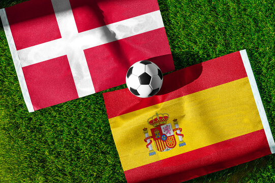 Denmark vs. Spain football match. National flags on green grass with soccer ball in the middle. Football background for international match.