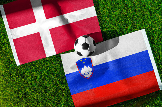 Denmark vs. Slovenia football match. National flags on green grass with soccer ball in the middle. Football background for international match.