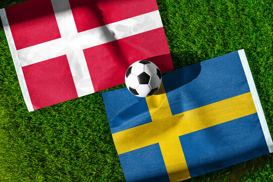 Denmark vs. Sweden football match. National flags on green grass with soccer ball in the middle. Football background for international match.