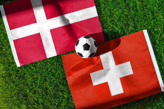 Denmark vs. Switzerland football match. National flags on green grass with soccer ball in the middle. Football background for international match.
