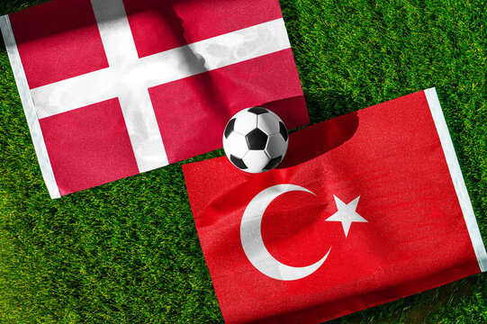 Denmark vs. Turkey football match. National flags on green grass with soccer ball in the middle. Football background for international match.