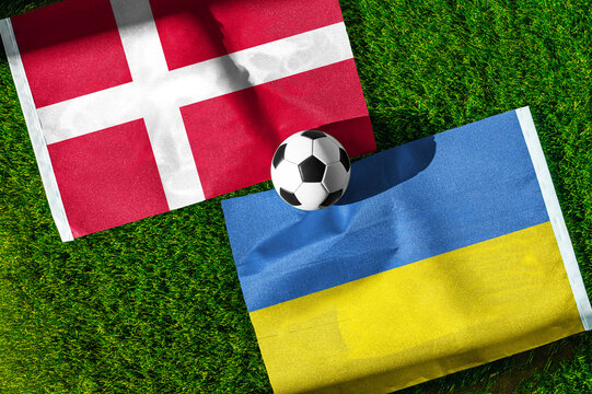 Denmark vs. Ukraine football match. National flags on green grass with soccer ball in the middle. Football background for international match.