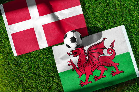 Denmark vs. Wales football match. National flags on green grass with soccer ball in the middle. Football background for international match.